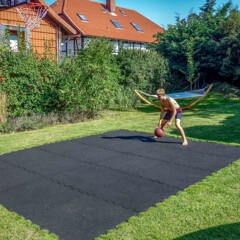 In den Rasen im Garten eines Wohnhauses ist ein Basketballplatz aus schwarzen Ballspielplatten von WARCO eingelassen. Ein Junge spielt darauf Basketball.