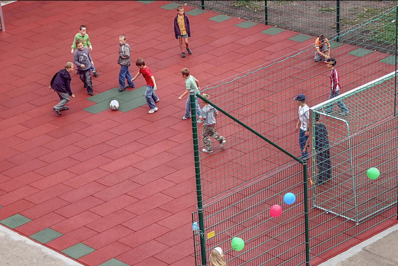 Les enfants jouent au foot sur un nouveau terrain de foot fait de dalles en caoutchouc rouges et vertes de WARCO.