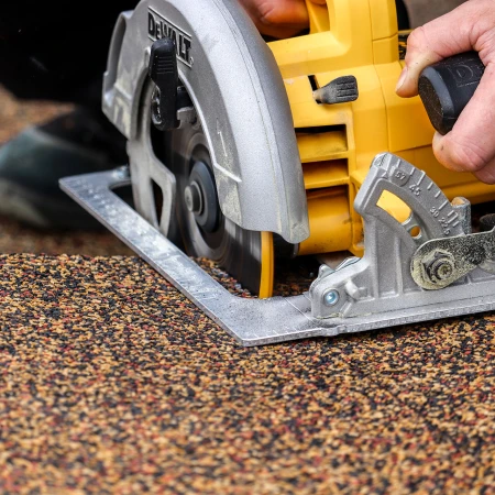 La scie circulaire manuelle avec une lame de scie à grosses dents pour le bois, coupe avec précision le long d’une ligne la dalle terrasse WARCO de granulat de caoutchouc.
