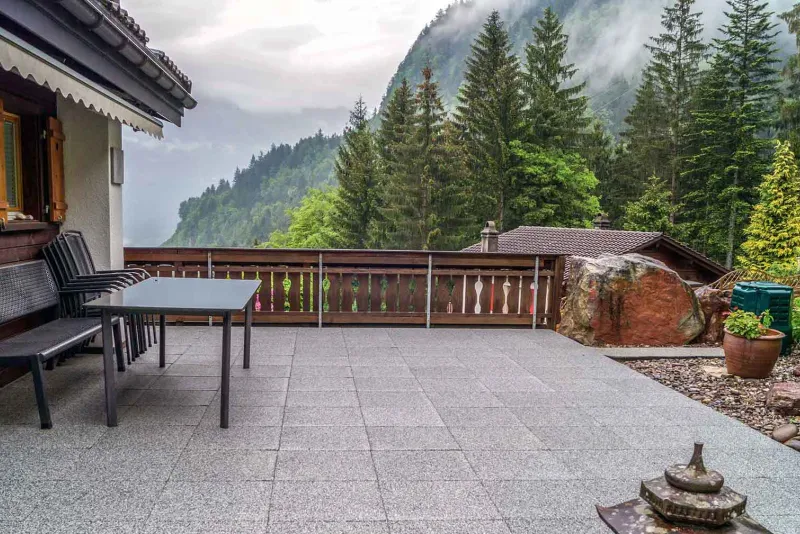 Sur fond d Alpes suisses, il y a un chalet avec une terrasse spacieuse couverte de dalles de terrasse WARCO en couleur granit clair.