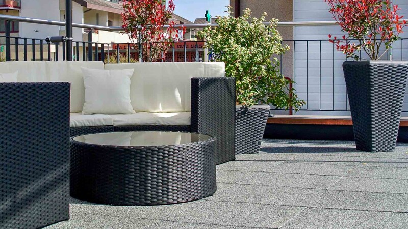 Sur un toit-terrasse ensoleillé, on peut admirer un salon fait de meubles en rotin avec le plancher WARCO en granit clair.