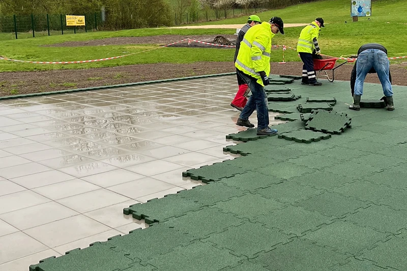 Un gruppo di operai posa le lastre esterne a clip di WARCO in colore verde erba sotto la pioggia in un'area piastrellata.
