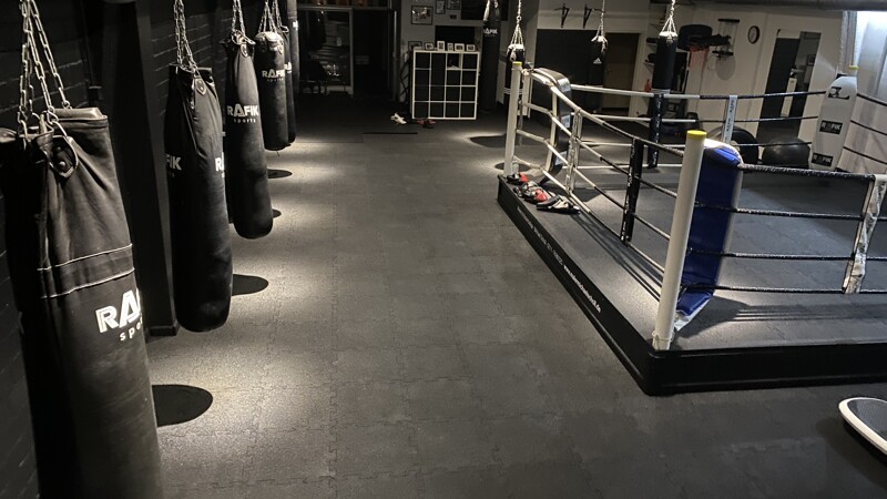 La salle de boxe avec les sacs de sable et le ring avec les tapis sportifs de WARCO en couelur Anthracite.