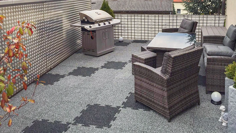 Cette photo montre une vaste terrasse sur toit équipée de dalles puzzle grises de WARCO. Leur surface antidérapante assure une bonne adhérence et un confort optimal. Des meubles en rotin résistants aux intempéries ainsi qu’un barbecue complètent l’aménagement et invitent à la convivialité. Ce revêtement robuste est facile à poser et idéal pour les espaces extérieurs grâce à son entretien minimal et sa résistance aux conditions climatiques. Un lieu accueillant pour se détendre et faire la fête.