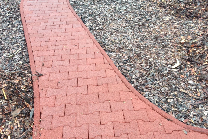 Eine roter Weg geht sich in leichten Kurven durch ein mit Pflanzen und Holzschnipseln gesäumtem Gelände.