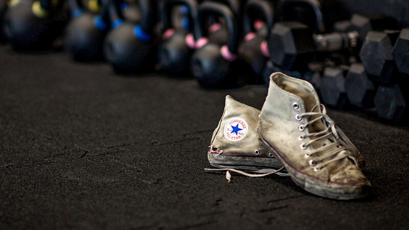Les Converse usées sur les tapis sportifs pour protection de sol WARCO en couleur Anthracite dans une salle de sport avec des haltères.