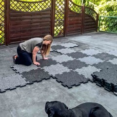 Auf einer mit Schweißbahnen abgedichteten Dachterrasse verlegt eine Kundin ihre WARCO Terrassenplatten TZ. Der Hund schaut dabei interessiert zu.