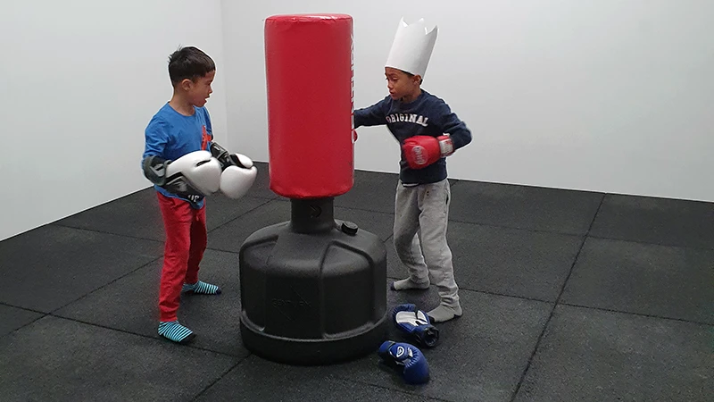 Due ragazzi fanno boxe sul sacco da boxe. Il pavimento per palestra WARCO in Antracite offre una buona protezione contro le cadute.