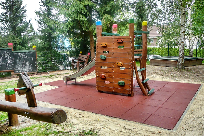 L'area giochi con una piccola torre di arrampicata e le lastre ammortizzanti WARCO. Intorno alla torre di arrampicata, è stata creata una zona di protezione anticaduta in conformità con gli standard attuali, utilizzando lastre rosse WARCO che assorbono gli urti.