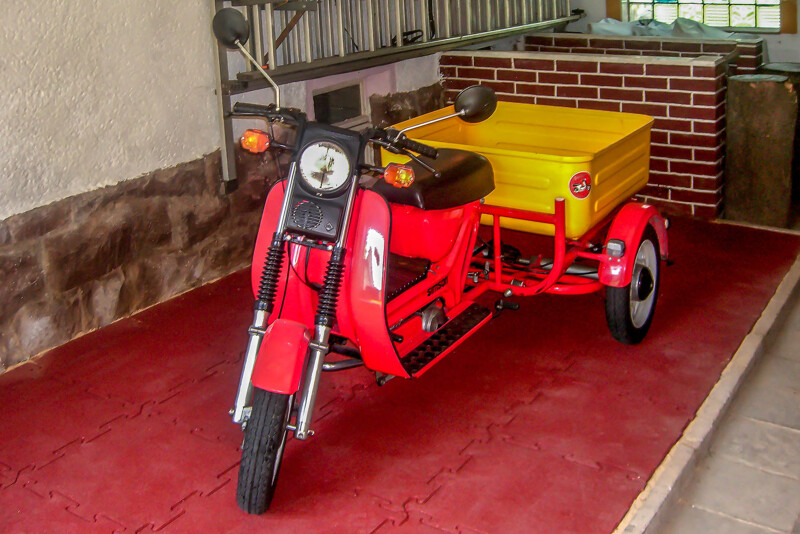 Un scooter avec remorque garé sur la place de stationnement recouverte de dalles rouges en granulat de caoutchouc WARCO.