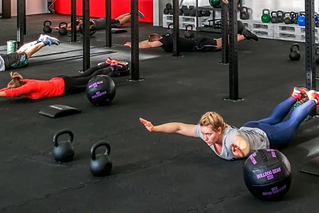 Le persone sdraiate sul pavimento scuro che si allenano in una palestra. Il pavimento è costituito da tappeti sportivi di protezione di WARCO.