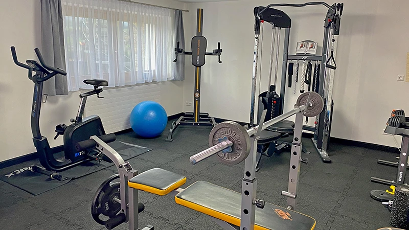 Dieses Homegym ist mit einem robusten schwarzen WARCO Fitnessboden ausgestattet, der aus ineinander greifenden Gummiplatten besteht. Der Boden bietet durch seine präzise Kantenverzahnung eine sichere und stabile Oberfläche, die für verschiedenste Trainingsgeräte geeignet ist. Das Fitnessstudio ist mit einer Hantelbank, Langhanteln, einem Heimtrainer und einem Multifunktionsgerät für Krafttraining ausgerüstet. Der strapazierfähige Boden von WARCO sorgt nicht nur für Komfort und Sicherheit, sondern schützt auch den Untergrund vor Beschädigungen, während er gleichzeitig die nötige Stoßdämpfung für effektive Workouts bietet.