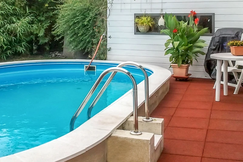 Le piastrelle per piscina antiscivolo e permeabile all'acqua WARCO in rosso mattone circondano la piscina fuori terra in giardino, garantendo la sicurezza in caso di caduta.