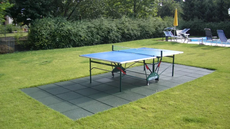 Les dalles sportives carrées WARCO en couleur vert gazon ont été installées sous la table de ping-pong dans le jardin.