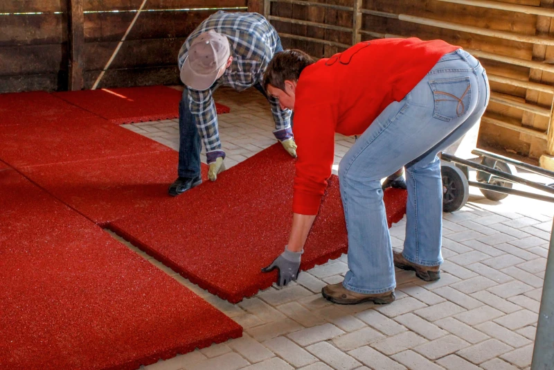 Due uomini posano i tappeti per scuderia WARCO di grande formato, antiscivolo e durevole nel box per cavalli con il pavimento in cemento.