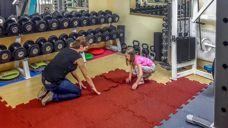 Une mère et sa fille posent les tapis de protection dans la salle de gym à la maison équipée du matériel de musculation.