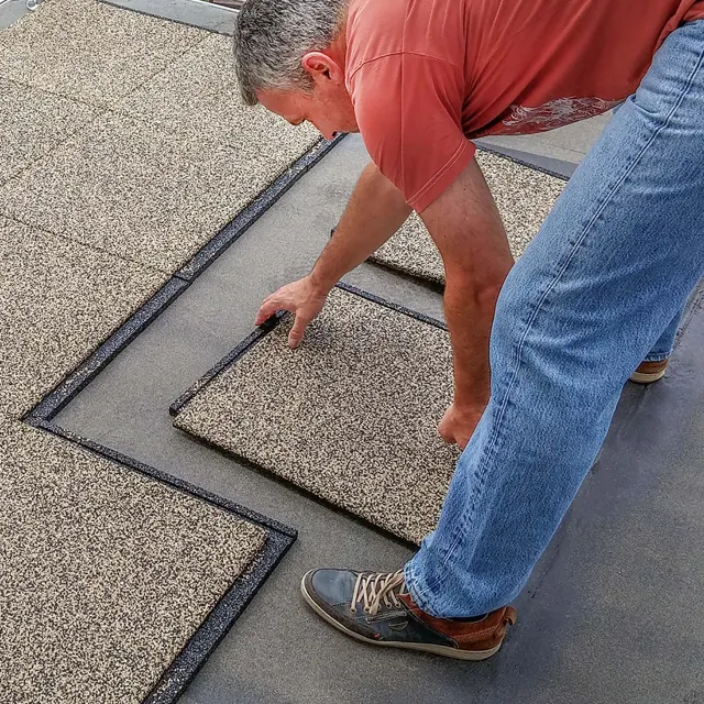 Un homme pose les dalles de terrasse WARCO directement sur une terrasse scellée et nivelée avec du feutre de toiture.