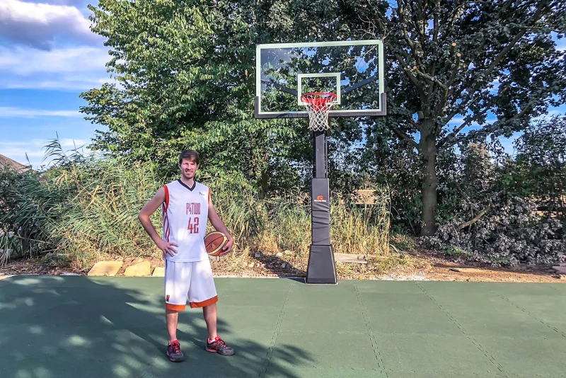 Sul campo da basket in giardino con le lastre per giocare a palla di WARCO in verde erba, c'è un alto giocatore di basket. Il buon rimbalzo della palla soddisfa i requisiti dei giocatori di basket.