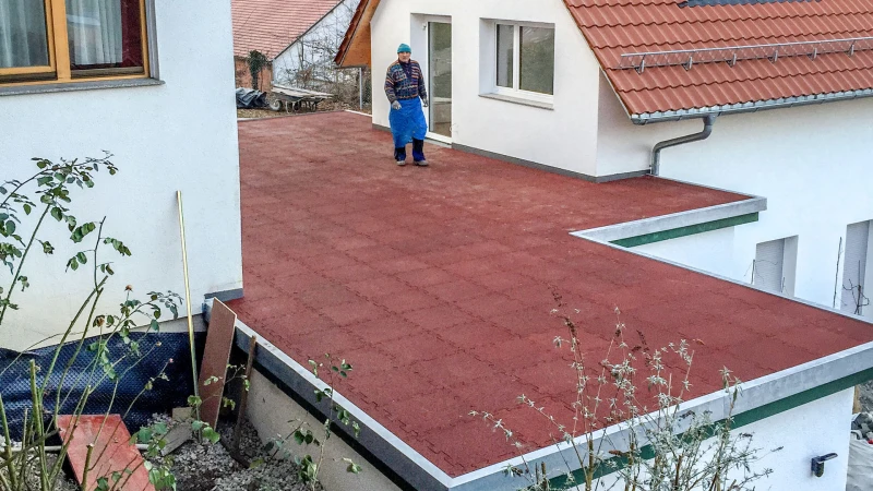 Tra due case unifamiliari, c'è un garage con un tetto piatto progettato come una terrazza fatta di lastre rosse WARCO.