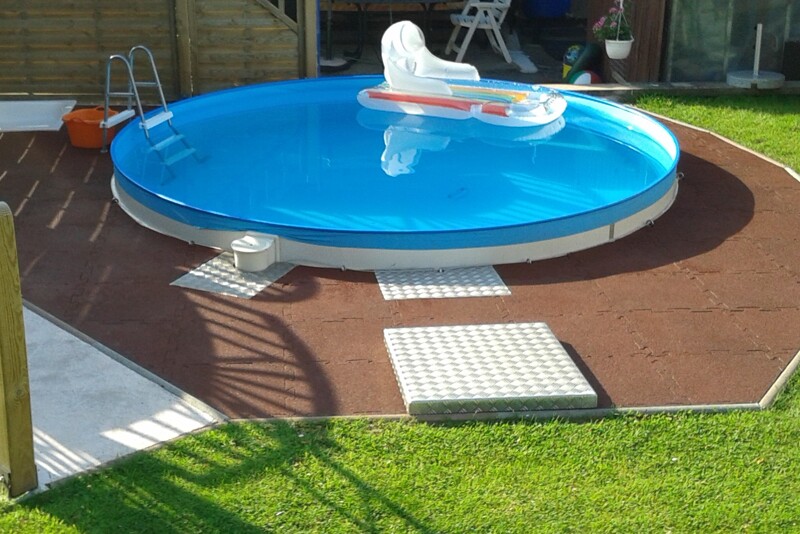 Dans un coin du jardin, le revêtement pour piscine WARCO est posé autour de la piscine ronde à moitié enfoncée dans le sol.