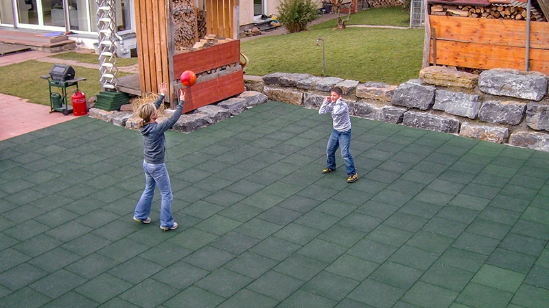 Una donna e un ragazzo giocano a pallavolo in un campo sportivo realizzato con le lastre verdi per giocare a palla WARCO nel giardino privato. Qualunque sia il tempo, il campo è aperto a tutti i tipi di attività sportive.