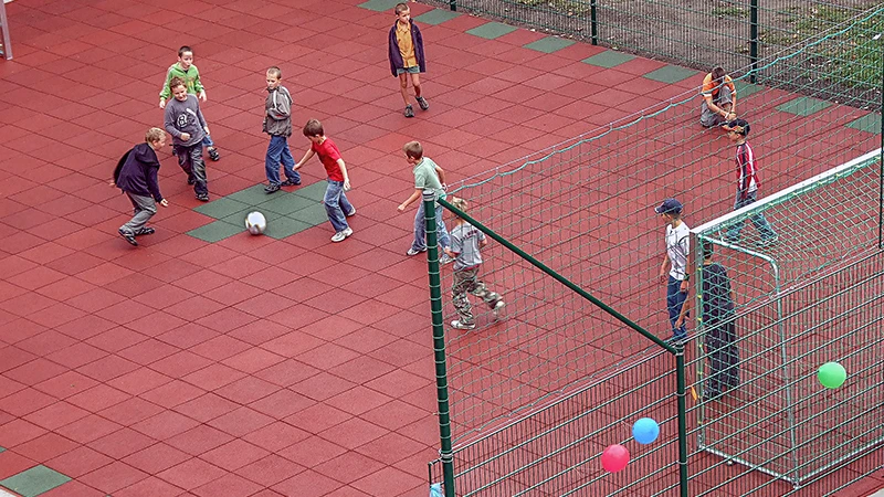 I bambini giocano a calcio sul nuovo campo da calcio della scuola realizzato con le lastre rosse e verdi per giocare a palla di WARCO.