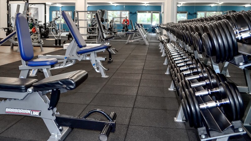 In einem Fitnessstudio sind mehrere Schrägbänke für das Kurzhanteltraining auf einem gut dämpfenden WARCO Fitness-Boden aufgestellt. Vor den Schrägbänken steht ein Regal mit Hanteln zum Training bereit.