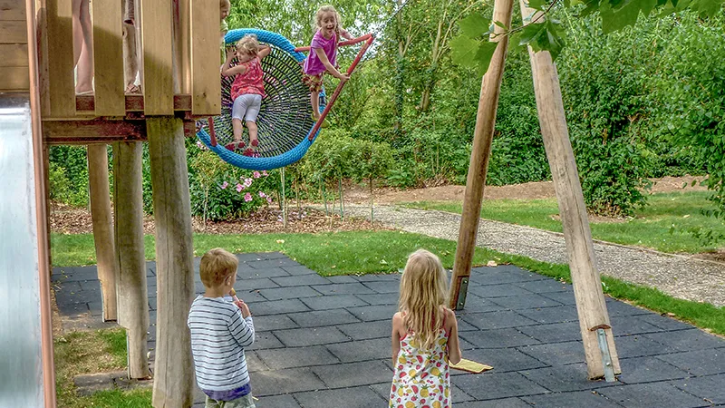 Fallschutzmatten unter einem Kletterhaus mit Rutsche und Nestschaukel auf dem Spielplatz.