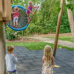 Fallschutzmatten unter einem Kletterhaus mit Rutsche und Nestschaukel auf dem Spielplatz.