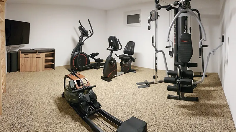 La palestra di casa con le attrezzature per l'allenamento con i pesi è rivestita con i tappeti sportivi tipo puzzle WARCO in colore Travertino.