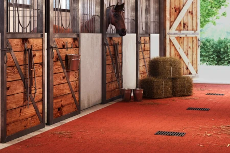 Le mattonelle autobloccanti WARCO rosse in granulato di gomma sono i pavimenti preferiti in un corridoio di una scuderia per cavalli.