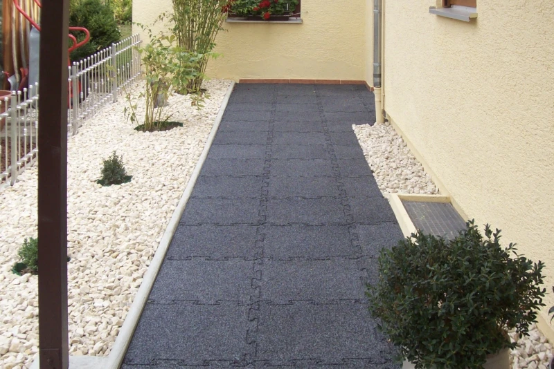 Un marciapiede in lastre di gomma WARCO in colore Antracite conduce attraverso il moderno ed elegante giardino alla porta d'ingresso.