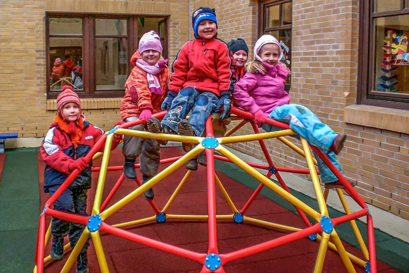 Les enfants sont assis sur la structure escalade sur une aire de jeux avec les dalles amortissantes aire de jeux rouges et verts de WARCO.